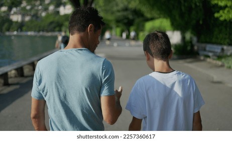 Parent giving life advice to teenager kid. Back of father and son walking together outside in park city. Dad talking to boy. manhood concept - Powered by Shutterstock