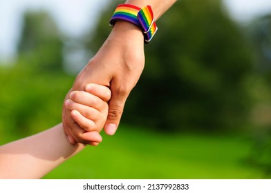 Parent Holds The Hand Of A Small Child. Mother Holding Baby's Hand. Rainbow Lgbt Bracelet On Parents Hand. 