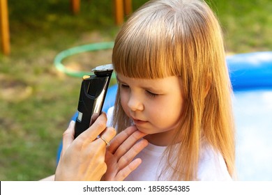 Parent, Mom Cutting Her Daughters Hair With An Electric Hair Trimmer, Using An Electrical Hair Clipper At Home. Amateur Simple Children Haircut, Corona Virus, Covid 19 Epidemic, Quarantine, Lockdown