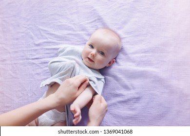 Parent Nurse Changing Diaper For Newborn Baby Daughter Son Child. Parent Babysitter Taking Care Of Child And Putting On Clothes Onesie. Authentic Lifestyle Candid Moment. Family Life Concept. 