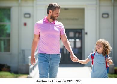 Parent and pupil of primary school go hand in hand. Teacher in t-shirt and cute schoolboy with backpack near school park.