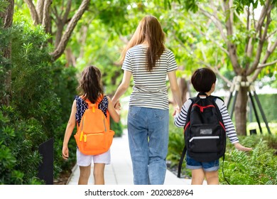 Parent And Pupil Of Primary School Go Hand In Hand. Woman And Kids With Backpack Behind The Back. Beginning Of Lessons.first Day At School.Mother Taking Daughter To School