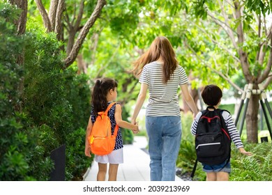 Parent And Pupil Of Primary School Go Hand In Hand. Woman And Kids With Backpack Behind The Back. Beginning Of Lessons.first Day At School.Mother Taking Daughter To School