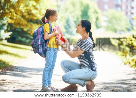 Parent and pupil of primary school go hand in hand. Woman and girl with backpack behind the back. Beginning of lessons. First day of fall.