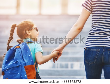 Parent and pupil of primary school go hand in hand. Woman and girl with backpack behind the back. Beginning of lessons. First day of fall.