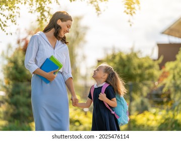 Parent And Pupil Of Primary School Going Hand In Hand. Woman And Girl With Backpack Behind The Back. Beginning Of Lessons.