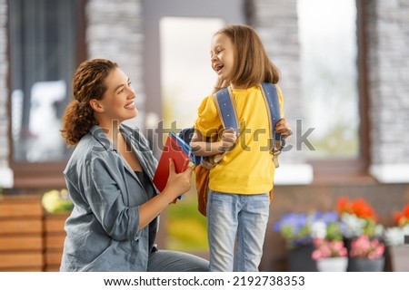 Parent and pupil of primary school going hand in hand. Woman and girl with backpack behind the back. Beginning of lessons.
