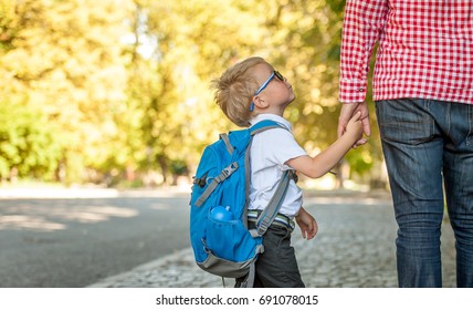 Parent Taking Child To School. Pupil Of Primary School Go Study With Backpack Outdoors. Father And Son Go Hand In Hand. Beginning Of Lessons. Back To School. First Day Of Fall. Elementary Student.