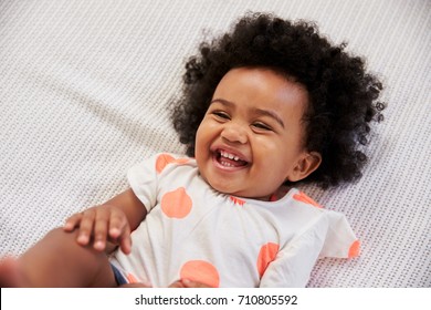 Parent Tickling Laughing Baby Girl Lying On Bed