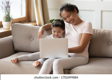 Parental Control And Educational Website Program Children Development Concept. Asian Mother Her Preschool Little Daughter Wear Comfy Home Clothes Relaxing On Couch With Laptop Having Fun Watch Cartoon