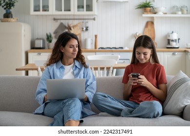 Parental monitoring of adolescents. Curious mother spying teenage daughter looking child text messages on smartphone. Mom and kid using gadgets, resting on sofa at home. Family and modern technologies - Powered by Shutterstock