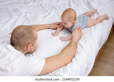 Parenthood and fatherhood. A young father supporting baby laying on the bed teaching him to lay on tummy and hold his head up and roll over on tummy. Baby care. Single father. Happy fathers day.