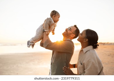 Parenting concept. Happy loving young parents playing with their little infant son on the beach, fooling and laughing, enjoying evening outside - Powered by Shutterstock