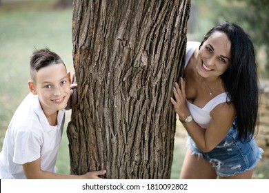 Parenting, Family And Single Parent Concept - A Happy Mother And Teen Son Smiling. Yung Mom And Teenage Son Stand Near A Tree In Park.