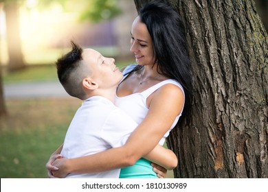 Parenting, Family And Single Parent Concept - A Happy Mother And Teen Son Smiling. Yung Mom And Teenage Son Stand Near A Tree In Park.