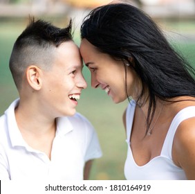 Parenting, Family And Single Parent Concept - A Happy Mother And Teen Son Smiling. Yung Mom And Teenage Son Look At Each Other And Laugh In Park.