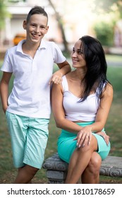 Parenting, Family And Single Parent Concept - A Happy Mother And Teen Son Smiling. Yung Mom And Teenage Son Look At Each Other And Laugh In Park.