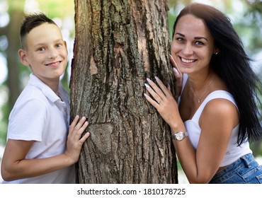 Parenting, Motherhood, Family Lifesstile And Single Parent Concept - A Happy Mother And Teen Son Smiling. Yung Mom And Teenage Son Stand Near A Tree In Park.