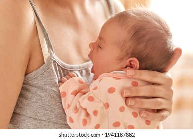 Parenting and new life, faceless mother holding newborn baby in her arms, unknown female wearing gray sleeveless t shirt posing with her tiny kid, child yawning.