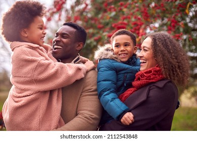 Parents Carrying Children As Family Enjoy Fall Or Winter Walk In Countryside