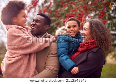 Parents Carrying Children As Family Enjoy Fall Or Winter Walk In Countryside