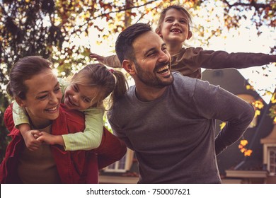 Parents carrying little girls on piggyback. - Shutterstock ID 750007621
