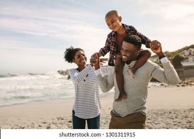 Parents carrying son on shoulders on beach vacation. African family of mother and father carrying son on his shoulders on vacation. - Powered by Shutterstock