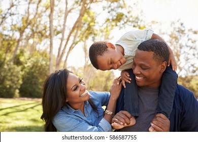 Parents Carrying Son On Shoulders As They Walk In Park