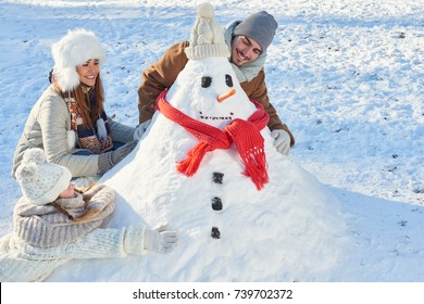 Parents And Child Build Snowman In Winter As A Family