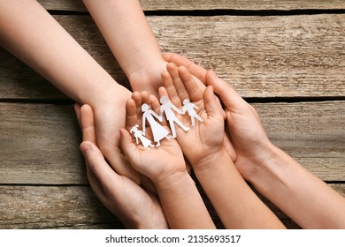 Parents and child holding paper cutout of family at wooden table, top view - Powered by Shutterstock