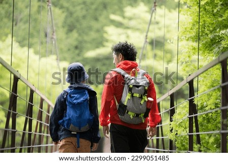 Parents and children go on a leisure trip to the fresh green mountains and cross the suspension bridge while talking happily. For summer vacation, outing expedition, etc.