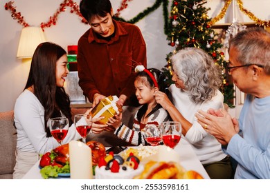 Parents, children, and grandparents gather at home for a joyful Christmas and New Year celebration, also marking the granddaughter’s birthday. They share wine, food, drinks, and exchange gift boxes - Powered by Shutterstock