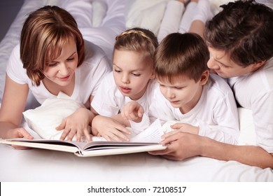 Parents Of Children Reading A Book In Bed