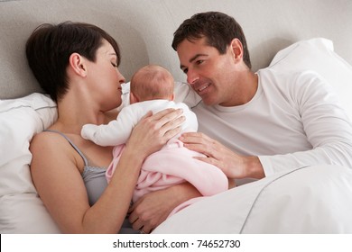 Parents Cuddling Newborn Baby In Bed At Home