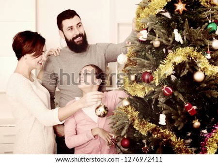 Parents and daughter putting decorations on Christmas tree at home
