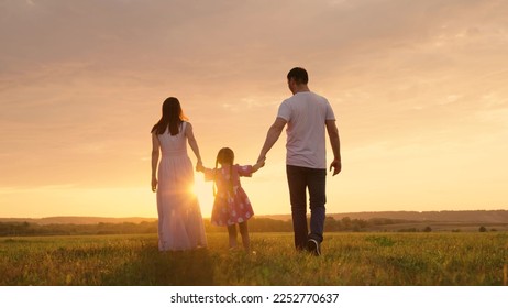 Parents, daughter run at sunset, kid holds hands of his parents and jumps. Active family playing in meadow with their daughter at sunset, teamwork. Happy family warm autumn day in park. Family, nature - Powered by Shutterstock