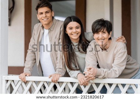 parents day celebration, middle aged woman hugging with cheerful daughter and son on porch of summer house, looking at camera, family reunion, bonding, modern parenting, moments to remember