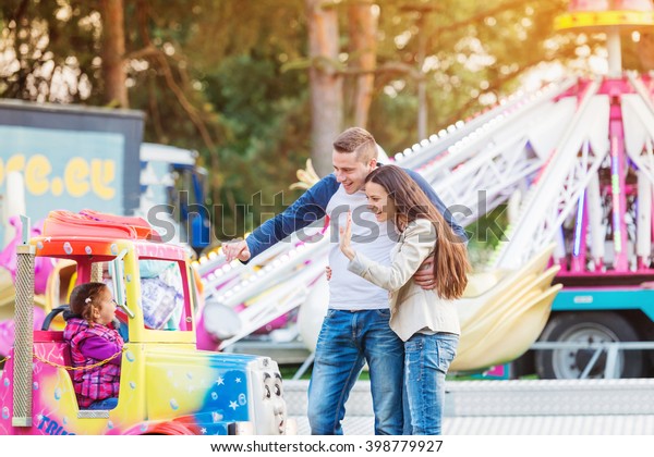 Parents at\
fun fair, waving their child taking\
ride