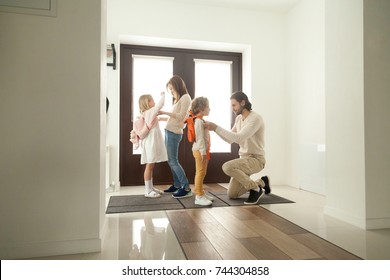 Parents Get Children Ready For School Standing At Hallway, Mother And Father Helping Little Preschool Kids Boy Girl Put Backpacks On At Home Hall, Mom With Dad Dressing Son Daughter In The Morning 