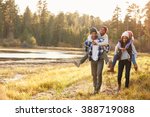 Parents Giving Children Piggyback Ride On Walk By Lake