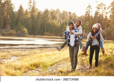 Parents Giving Children Piggyback Ride On Walk By Lake