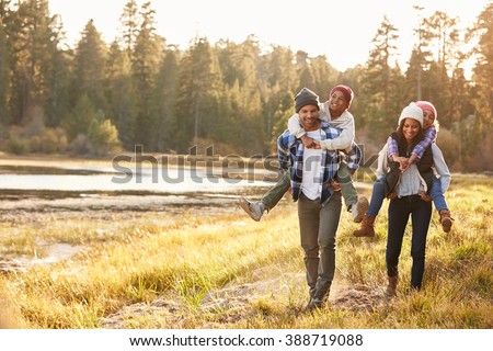 Parents Giving Children Piggyback Ride On Walk By Lake