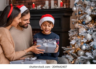 Parents giving present their son while sitting near Christmas tree in living room. Little boy opening Christmas present, Happy New Year and Merry Christmas - Powered by Shutterstock