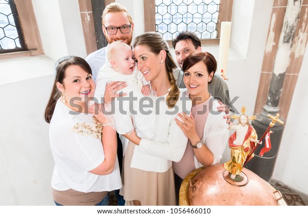 Parents and godparents stand at the baptismal font\
with the baby in a\
church