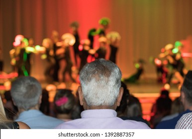 Parents And Grandparents In An Audience Hall Watching A Children Performance On A School Theater Stage. Concept: Big Evening Event Is On An Open Day At School.