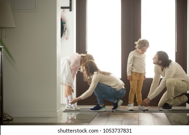 Parents helping children son and daughter put shoes on or take off in hall getting ready to go out together or coming back home from walk, care and good relations in happy family with kids concept
