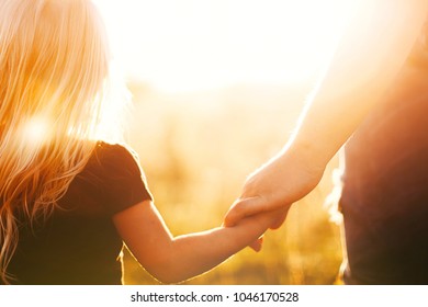 Parents Hold The Hand Of A Small Child At Sunset