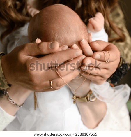 The parents hold the tiny head of their child in their hands, a gold cross and chain, jewelry hangs on their hands.