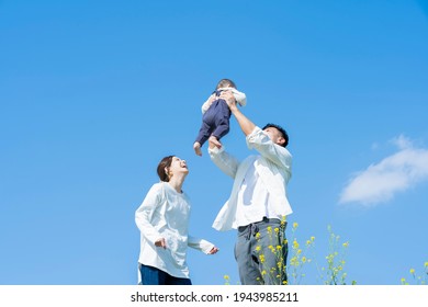 Parents Holding Their Baby High Under The Blue Sky