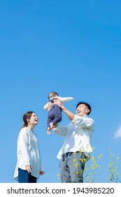 Parents Holding Their Baby High Under The Blue Sky